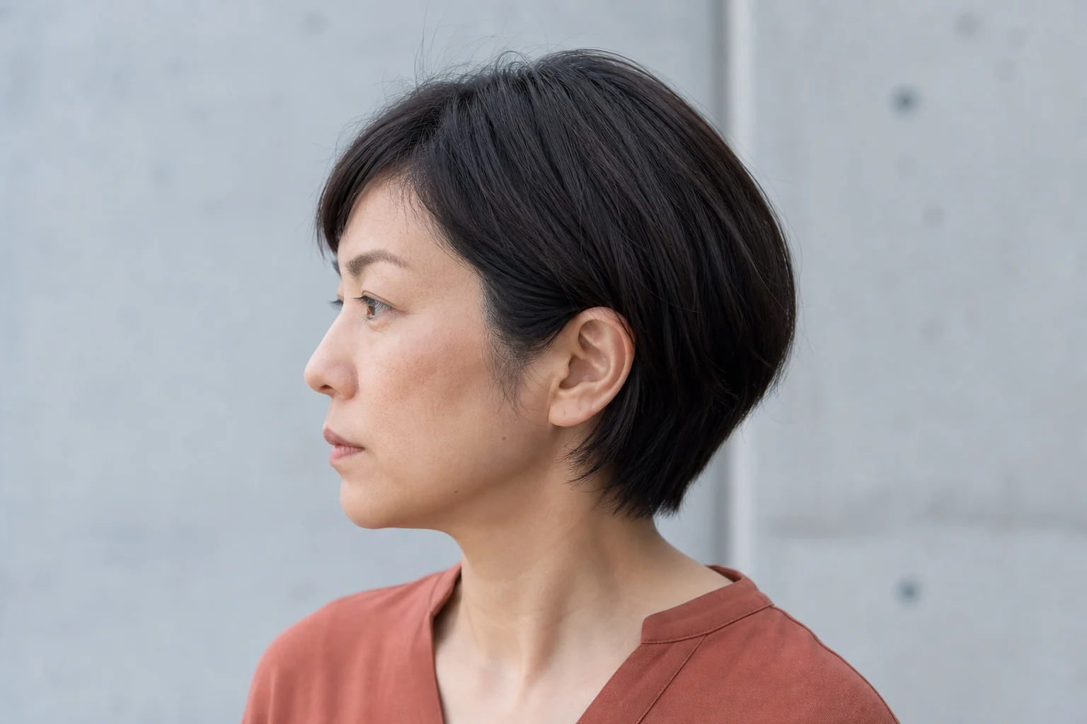 前髪なしショートのトップからこめかみと耳周りへつながる毛流れを左横顔で見せる成人女性