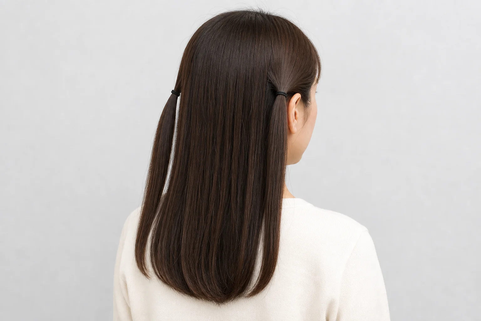 肩下の暗い髪の両サイドを耳後ろで別々の黒いゴムに結んだ後ろ姿
