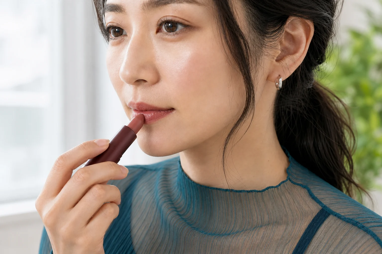 ローズブラウンのスティック口紅を下唇中央へ軽く重ねる成人女性
