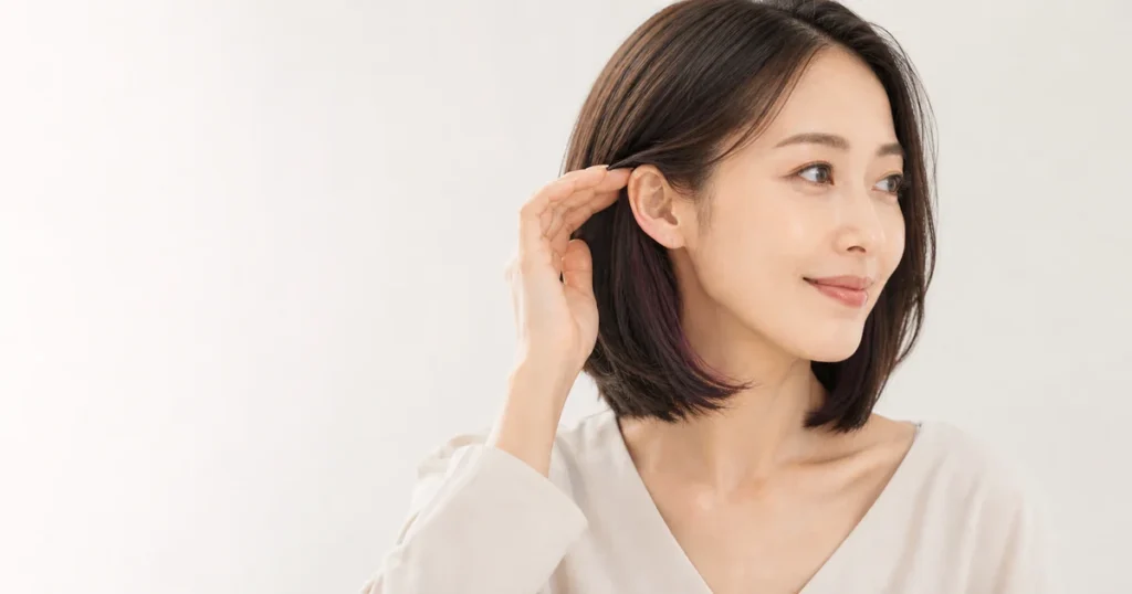 耳にかけた暗いボブの内側に深いカシスブラウンが見える成人女性