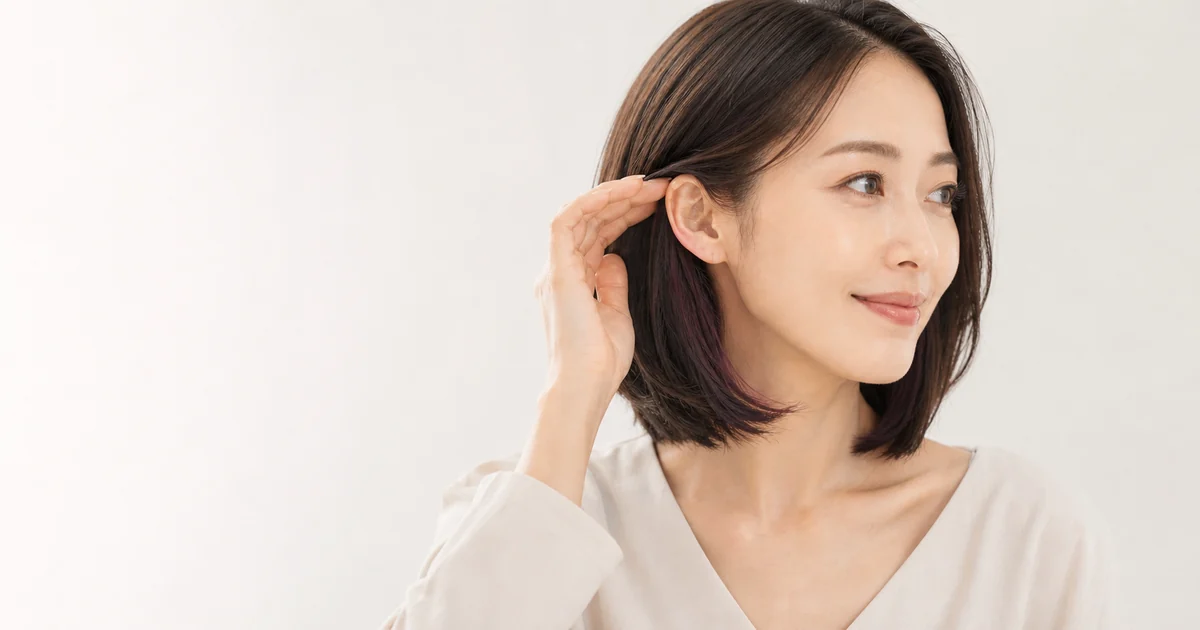 耳にかけた暗いボブの内側に深いカシスブラウンが見える成人女性