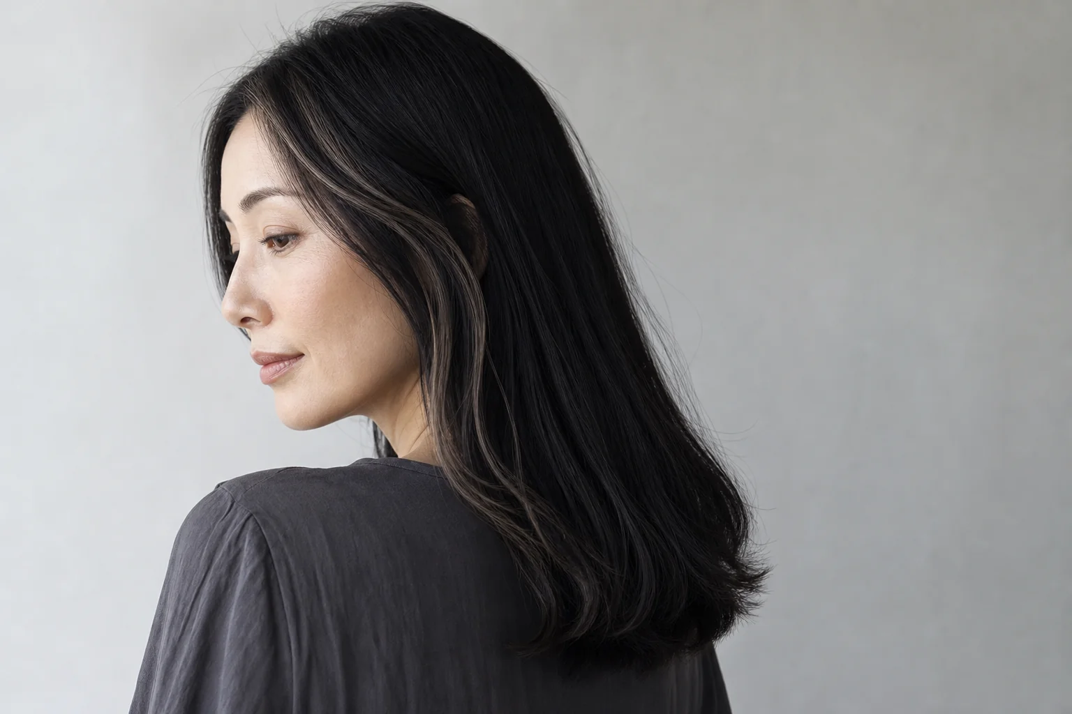 鎖骨下の黒髪の顔まわりへ細いスモーキーベージュハイライトを入れた成人女性