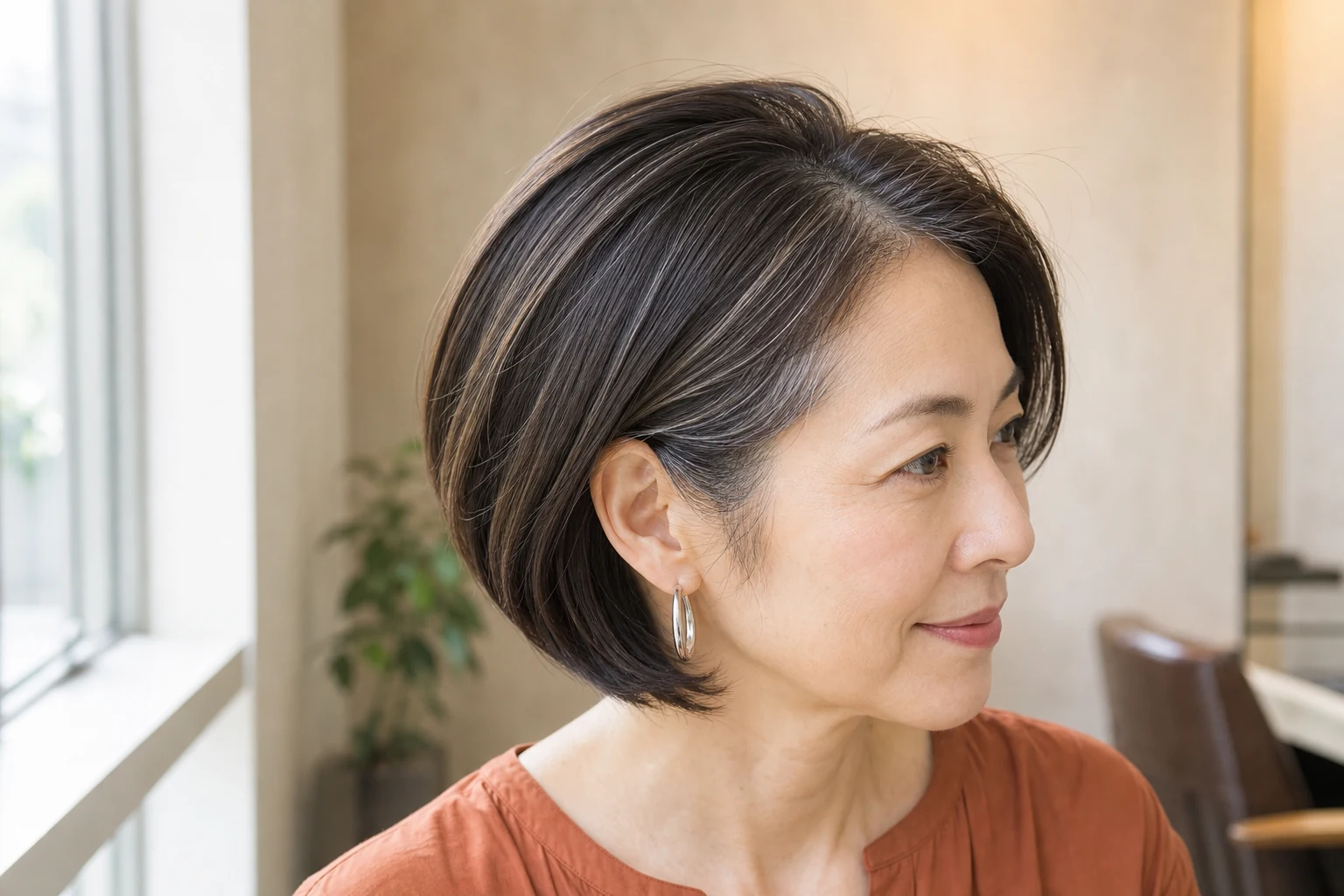 こめかみの白髪と細いクールベージュの筋を残したあご下ボブの成人女性