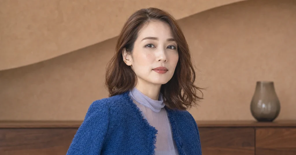 低彩度のカーキを目尻側へ薄く入れ、ピーチベージュの頬と赤みブラウンの唇を合わせたウェーブヘアの成人女性