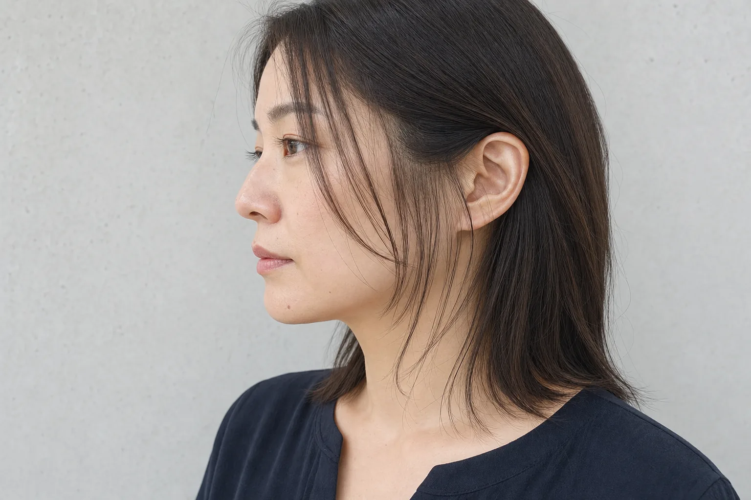 左横顔でこめかみから細い毛束を複数の長さへつないだ暗髪ロングの成人女性