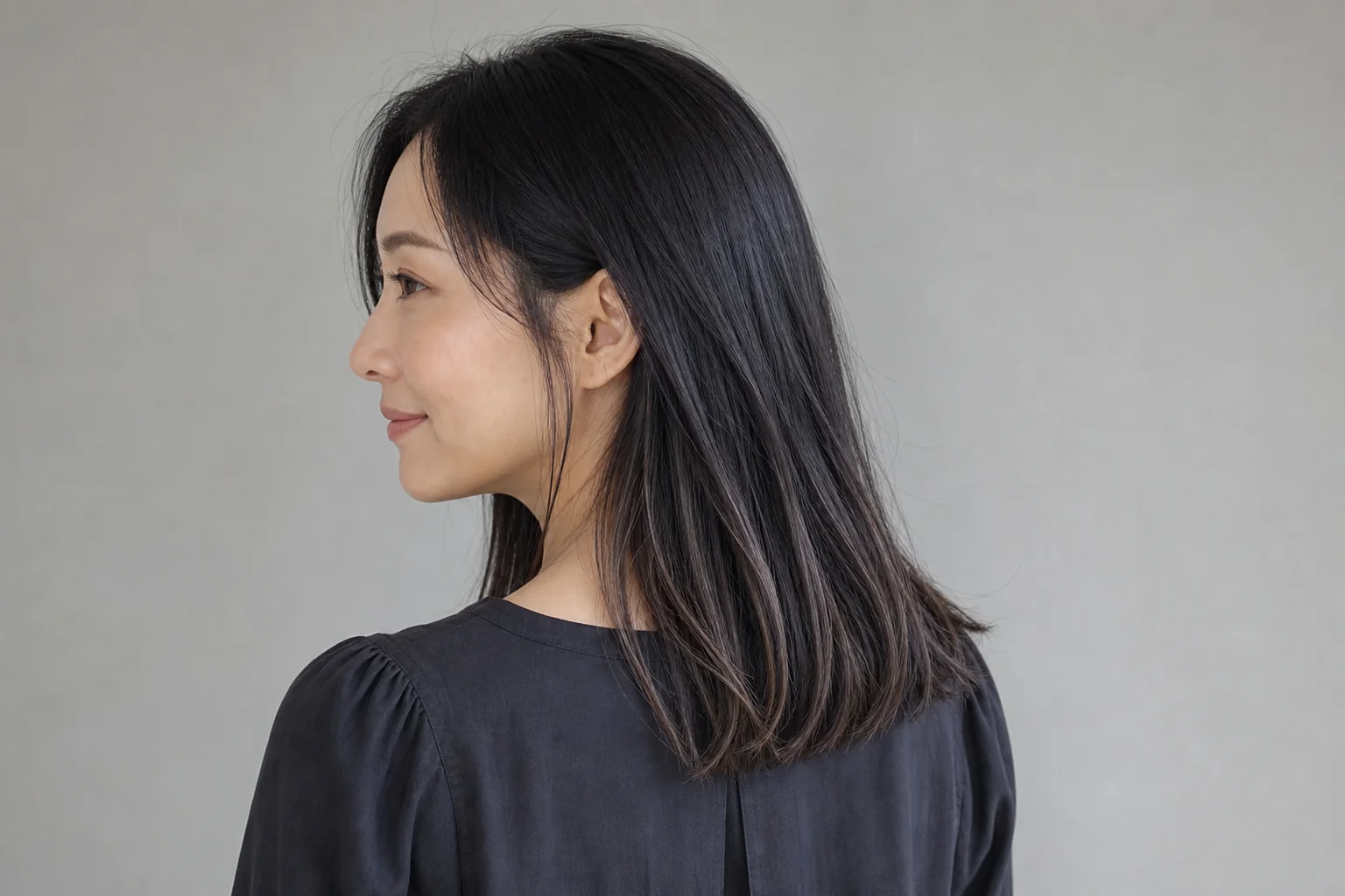 鎖骨下の黒髪の耳後ろから低い位置へ細いトープブラウンハイライトを入れた成人女性