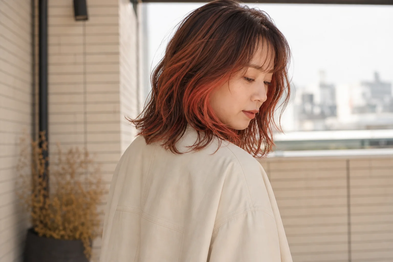 暖色ブラウンの影とシアーなバーミリオンオレンジが見える肩丈ウェーブヘアの成人女性