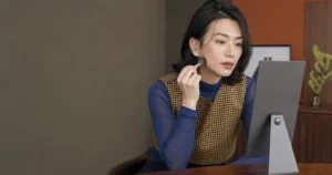 コバルトのシアートップスとチェックベストを着て鏡を見ながらブラシを頬へ当てる成人