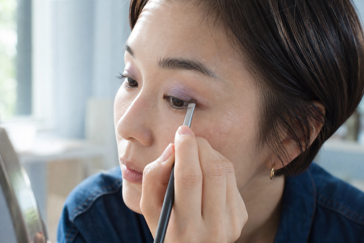 細いブラシで上まぶたのキワへグレージュを置く30代女性
