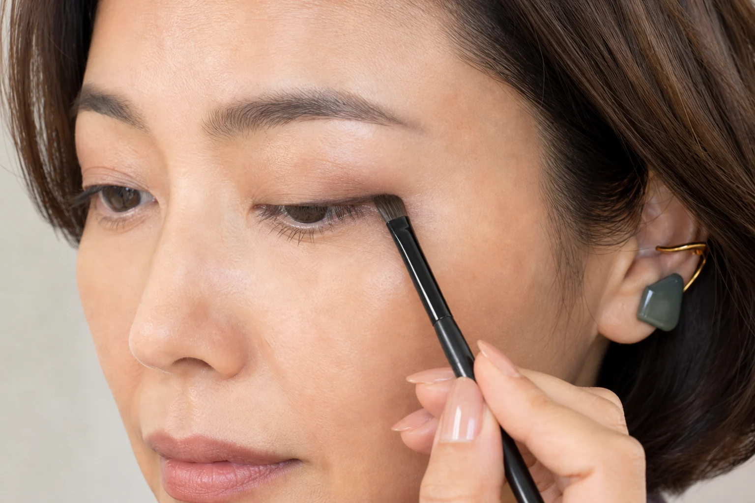 上まつ毛の中央から目尻側のキワへ深いブラウンの締め色を平筆で細く置く40代前半の成人女性
