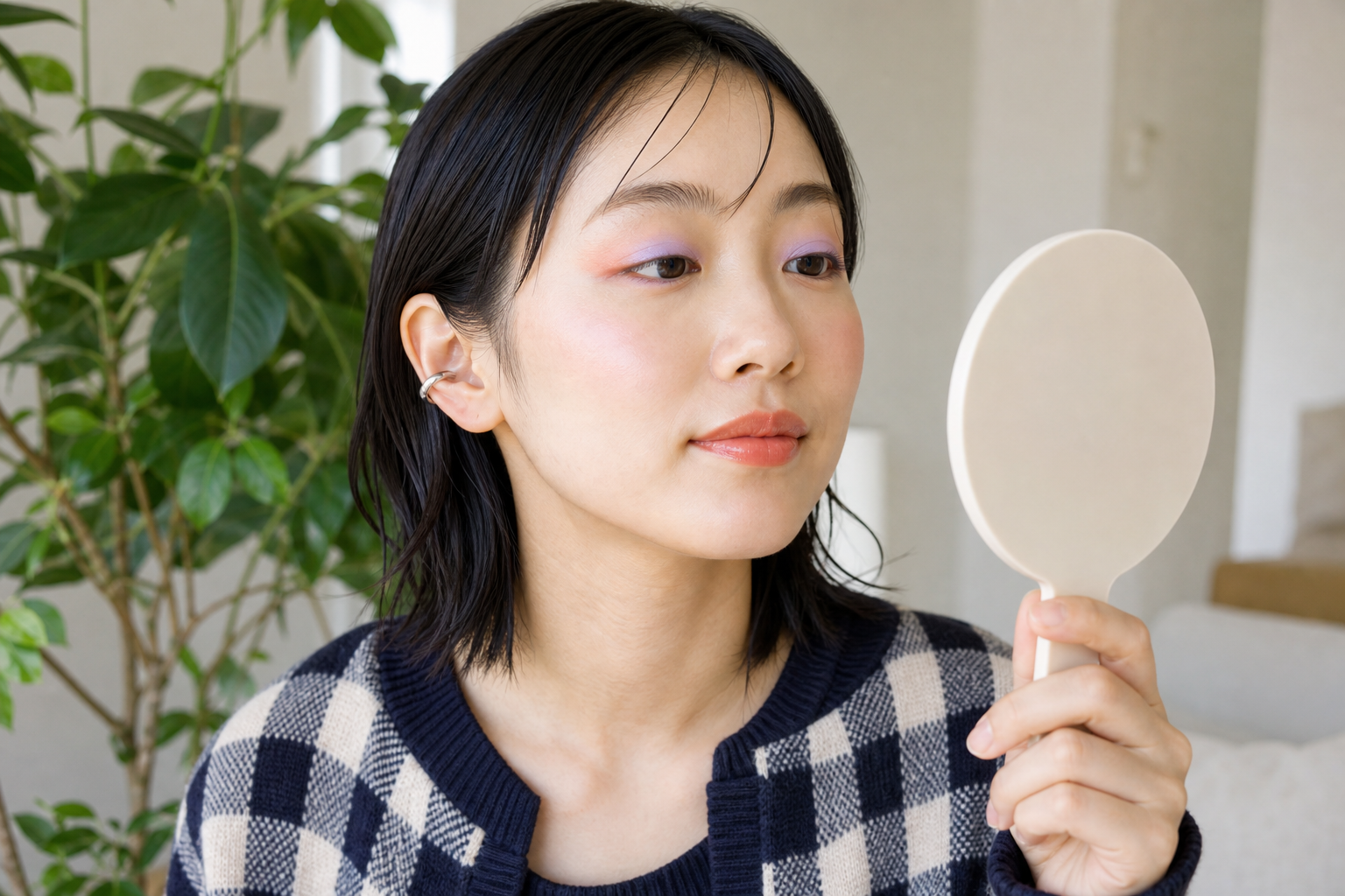 淡いパステルアイとシアーコーラルリップの全体バランスを鏡で確認する女性