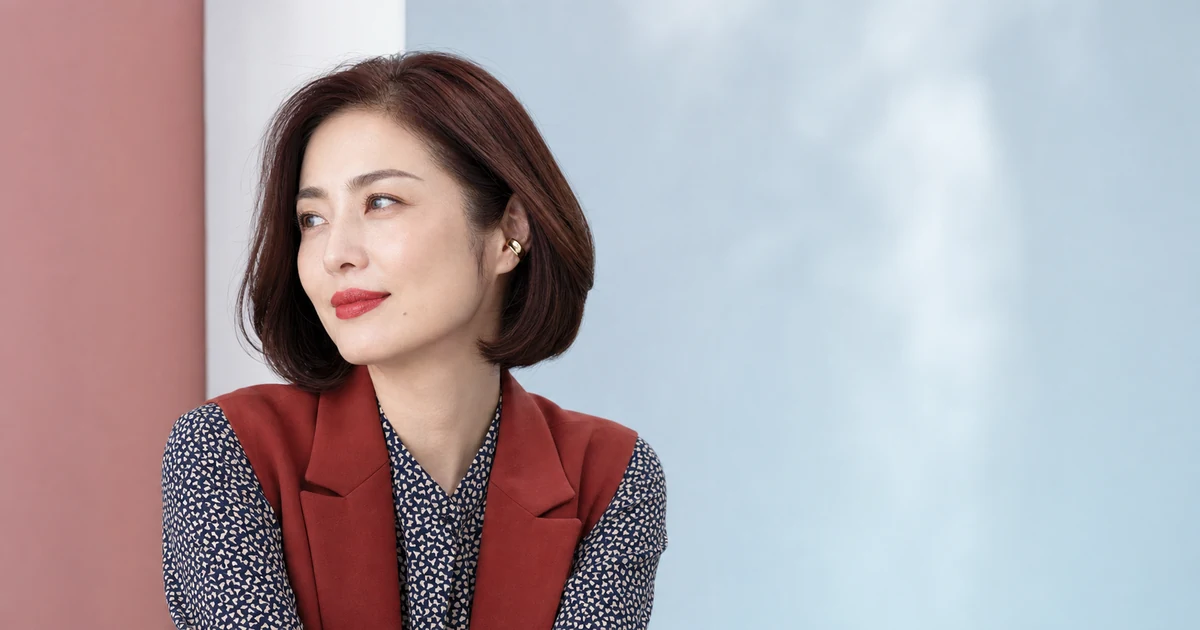 赤いリップと自然なグレーブラウン眉を合わせ、ブリックレッドのベストを着た成人女性