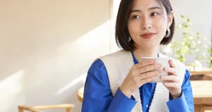 細いゴールドテープを密着させたシアーブラッシュネイルでカップを持つ30代女性